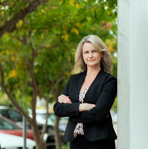 Branwen Morganstanding with arms folded leaning against a wall. 