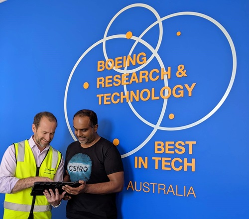 Two men with an ipad in front of the Boeing logo