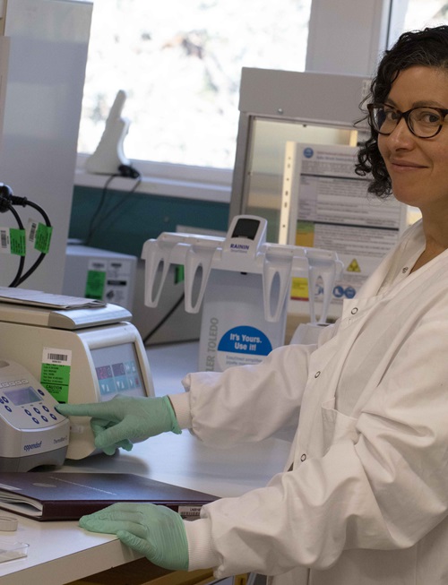 A woman standing at a laboratory bench, pushing a button on a piece of equipment used for her experiments.