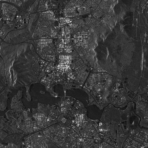 Synthetic Aperture Radar satellite image of Canberra showing dark areas such as Lake Burley Griffin and the roads. Buildings show up white-grey, while other features are revealed in various shades of grey.