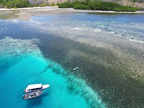White boat on crystal blue coloured water with an island in the foreground.
