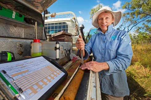 Man in a blue shirt and a floppy brown hat standing at his utility vehicle with soil testing equipment under a canopy on the back of the vehicle