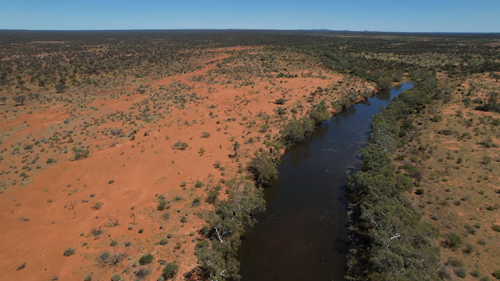 Red dirt desert and a river bordered by green gum trees.
