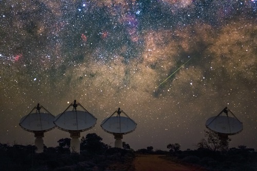For dish antennas are aligned along the horizon under a starry sky.