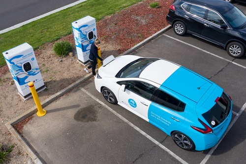 Person stands next to electric car as it charges.