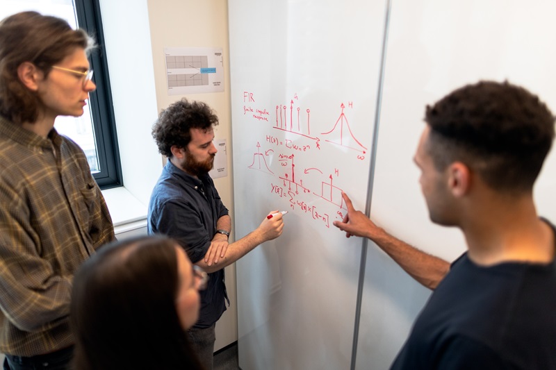 Four people standing at a whiteboard, working together on a research problem. 