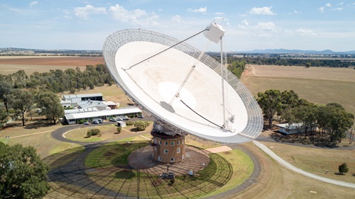 A large dish antenna sits in a large green field and points to the sky