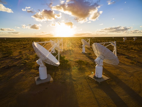 Dish antennas are spread across the outback, with the sun rising behind them