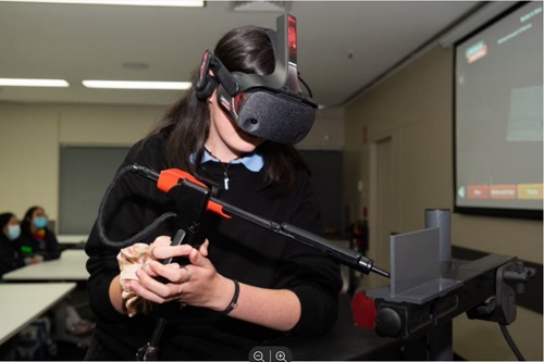 Student with a VR headset over their head and a controller, which they are holding in both hands.