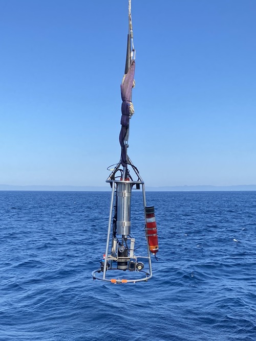 A piece of scientific equipment suspended over the ocean from a wire.