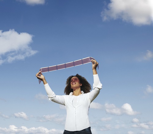 Person holding a strip of printed flexible solar cells above their head towards to sun. 