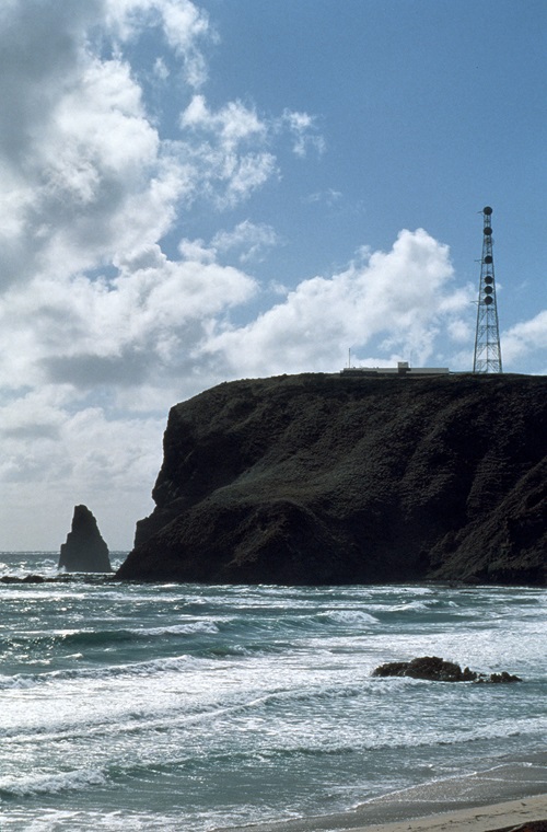 a large cliff face surrounded by ocean. there is some research infrastructure (e.g. a tower) in sillouhette.