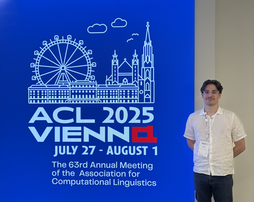 Aaron Nicolson standing beside a banner with the words ACL 2025 Vienna.