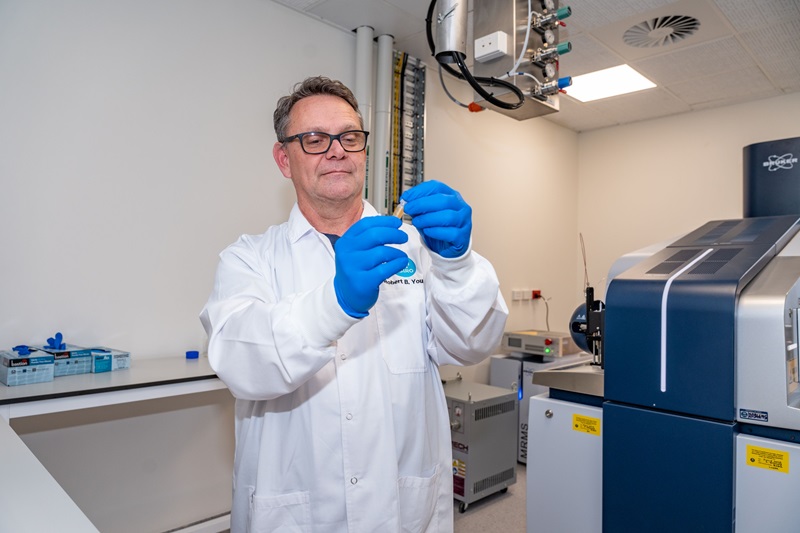 Robert Young in a lab coat and blue protective gloves examining a piece of equipment in the ICR facility