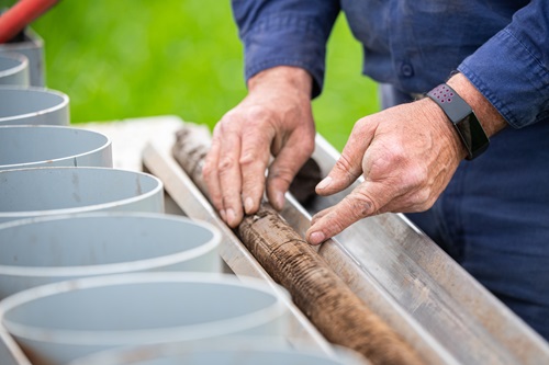 A close up of a soil core laid out with a scientist inspecting with hands and buckets in the foreground for samples