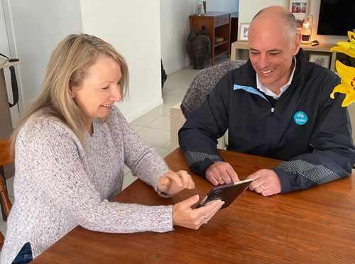 A woman points to a phone while seated next to a man at a table. 