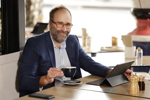 A man with glasses holding a coffee cup and a tablet. 