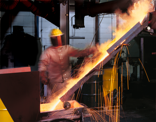 Person in a heat protection suit and mask pouring metal in a furnace