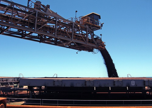 A mine site with the photograph taken looking up at a large metal arm with conveyor belt pouring ore.