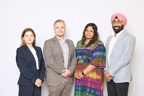 Four people standing in a row with a blank background facing the camera.