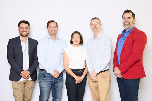 Five people standing in a row against a blank background, facing the camera.