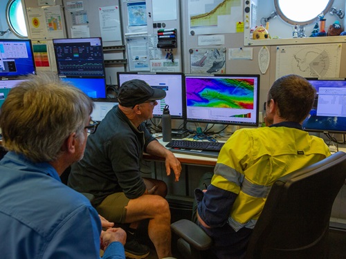 Three people studying screens planning survey sites from seafloor mapping. 