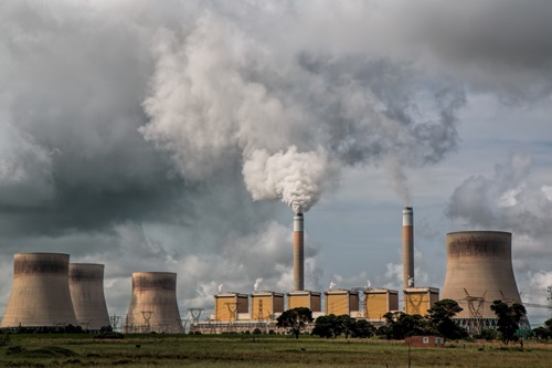 power station with large chimneys, two releasing clouds of smoke against a grey sky