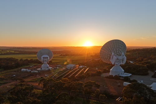ESA's New Norcia ground station in Western Australia, two large antennas are show facing the sunset, amongst the hills. 