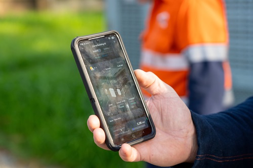 hand holding a mobile with someone in the background wearing an orange and high via work top