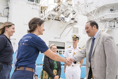 Two people shaking hands in front of several other people.