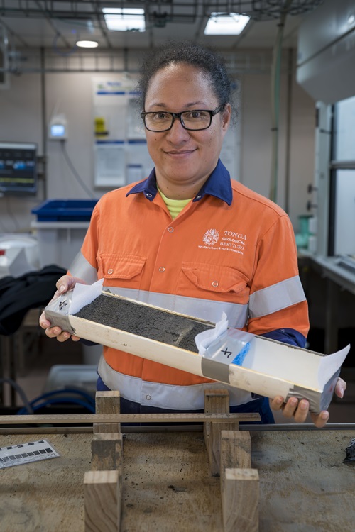 A person in a hi vis shirt holding a PVC tube filled with what looks like dirt.