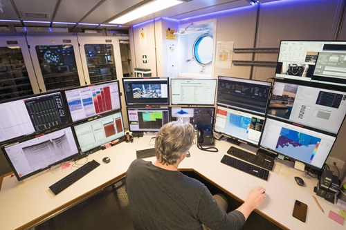 A person sitting in a chair looking at a bank of computer monitors on a desk.