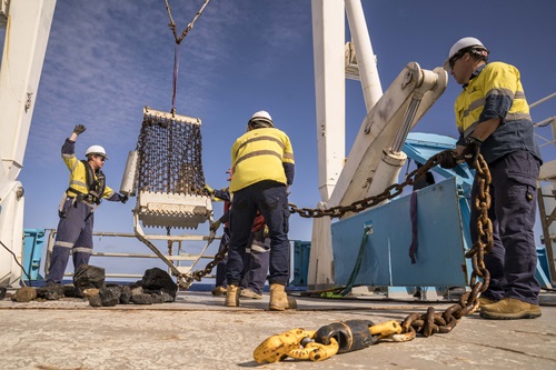 Three people haul in a piece of scientific equipment from the ocean and onto the back deck of a ship.