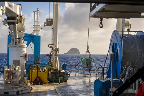 A piece of scientific equipment sits amongst other equipment on the back deck of a ship at sea.