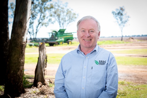 Man standing in front of grain harvester with paddock in distance.