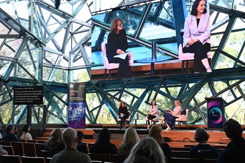 Cathy Foley AO PSM, Australia’s former Chief Scientist, and Dr Kate Cornick, Tech Council of Australia, sitting on a stage in a 'fireside chat' hosted by Tenille Eyre, projected on a larger screen above in an open conference hall 
