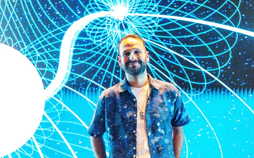 Person standing in front of a glowing, abstract display of intersecting light paths and data-like patterns, representing astronomical networks.