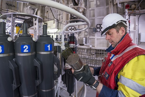 A person in a hard hat and life preserver looks at a piece of scientific equipment in a laboratory.