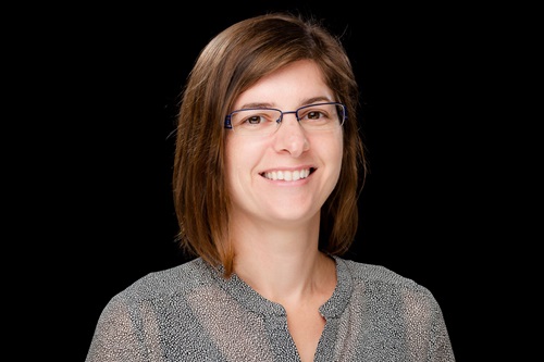 A headshot of a person standing in front of a black background.