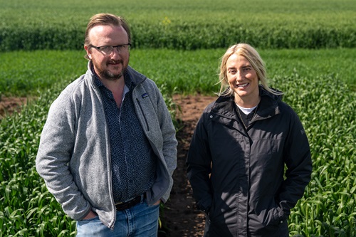 Dr Mark Farrell and Dr Jade Rose stand side by side in a green cereal crop, hands in their pockets, smiling at the camera. 
