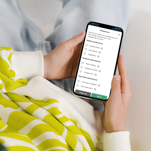 A person is holding a smartphone displaying a preferences screen from the CSIRO Total Wellbeing Diet app. 