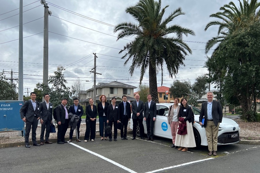 Group of people standing in a car park next to an electric vehicle. 