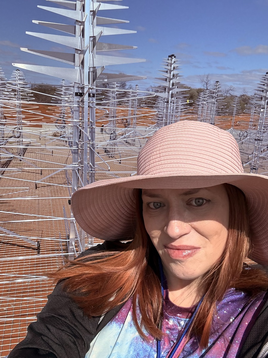 Woman in a broad-brimmed hat smiles at the camera. There are radio antennas behind her.
