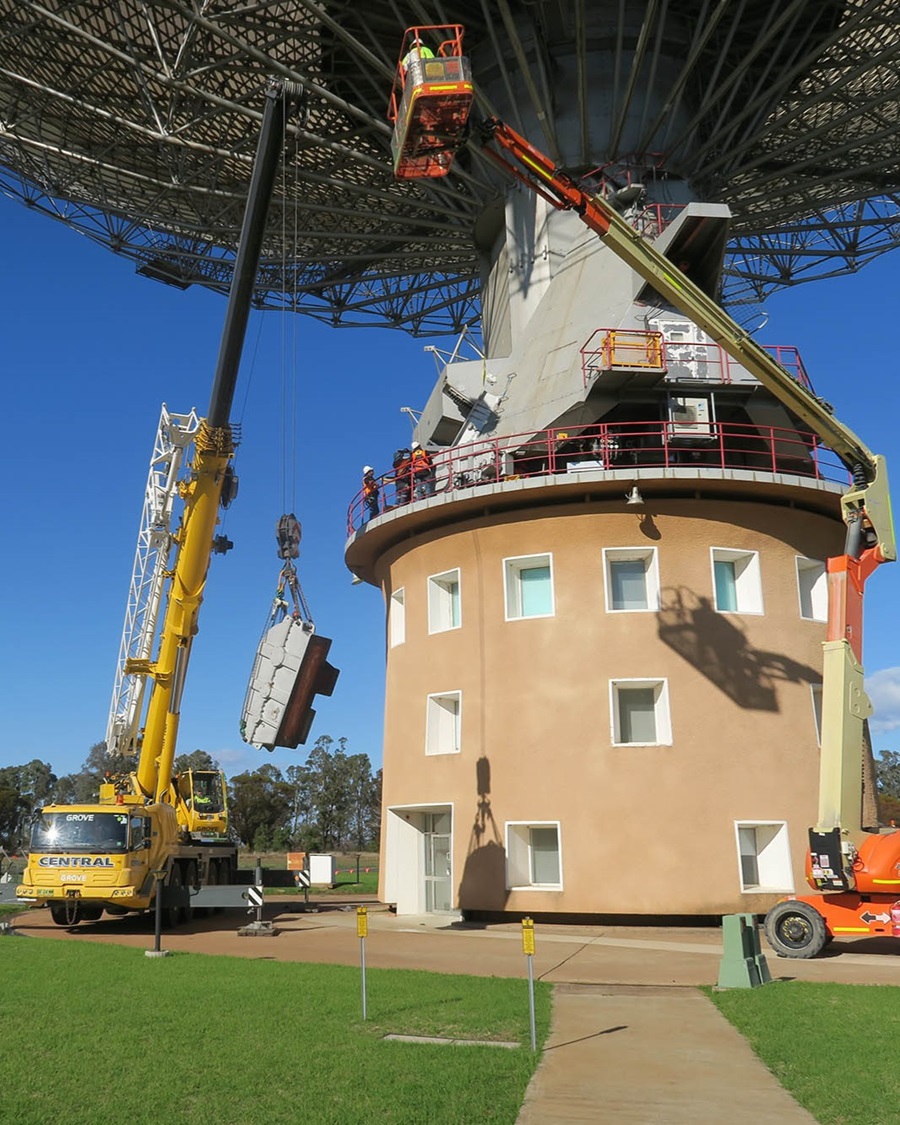 A crane and a cherry picker gentle manoeuvre a large gear box from under a dish telescope