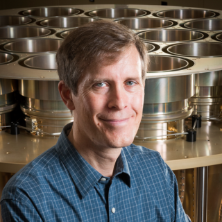 Douglas Bock is wearing a smart blue-green shirt and smiling at the camera.