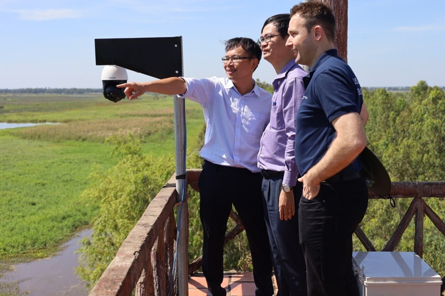 Three people standing on an observation platform overlooking forest and wetlands. 
