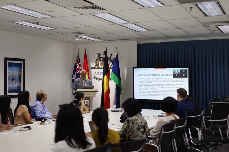 Person standing at a lecturn giving a presentation to a group of people sitting around a large conference table. 