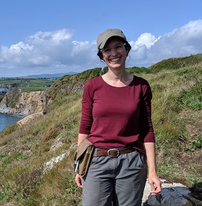 Smilling woman wearing cap with tools fixed ion belt standing on coastal cliff