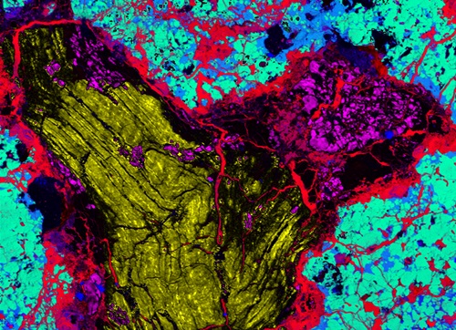 : Ureleite meteorite cross-section as seen by CSIRO's electron probe microanalyser (EPMA). Different materials are given different colours, with a large section of lonsdaleite in yellow in the middle left. At middle right is a small section of diamond in pink, Iron, in red, surrounds both. Magnesium in green and silicon in blue can be seen on the outside edges.