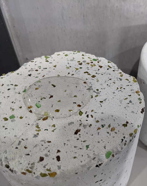 A  close-up view of a sample of the Tecoblock that shows the glass aggregate and the water on top demonstrates how it repels water. Image courtesy of Casafico